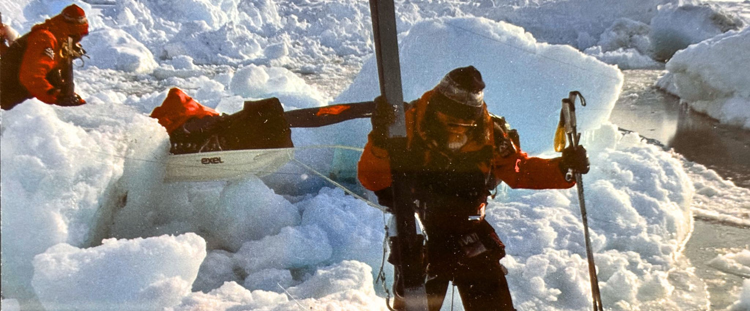 Drei Personen in Winterausrüstung bewegen sich in eisigem Gelände, wobei eine Person Skier trägt und die andere einen Schlitten durch Schnee und Eis zieht.