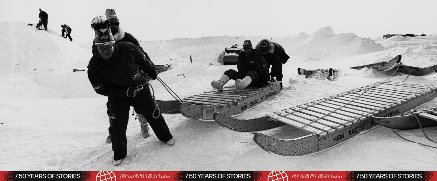 Vier Personen in Winterkleidung bereiten Holzschlitten in einer verschneiten, vereisten Landschaft vor, im Hintergrund sind Geräte zu sehen.