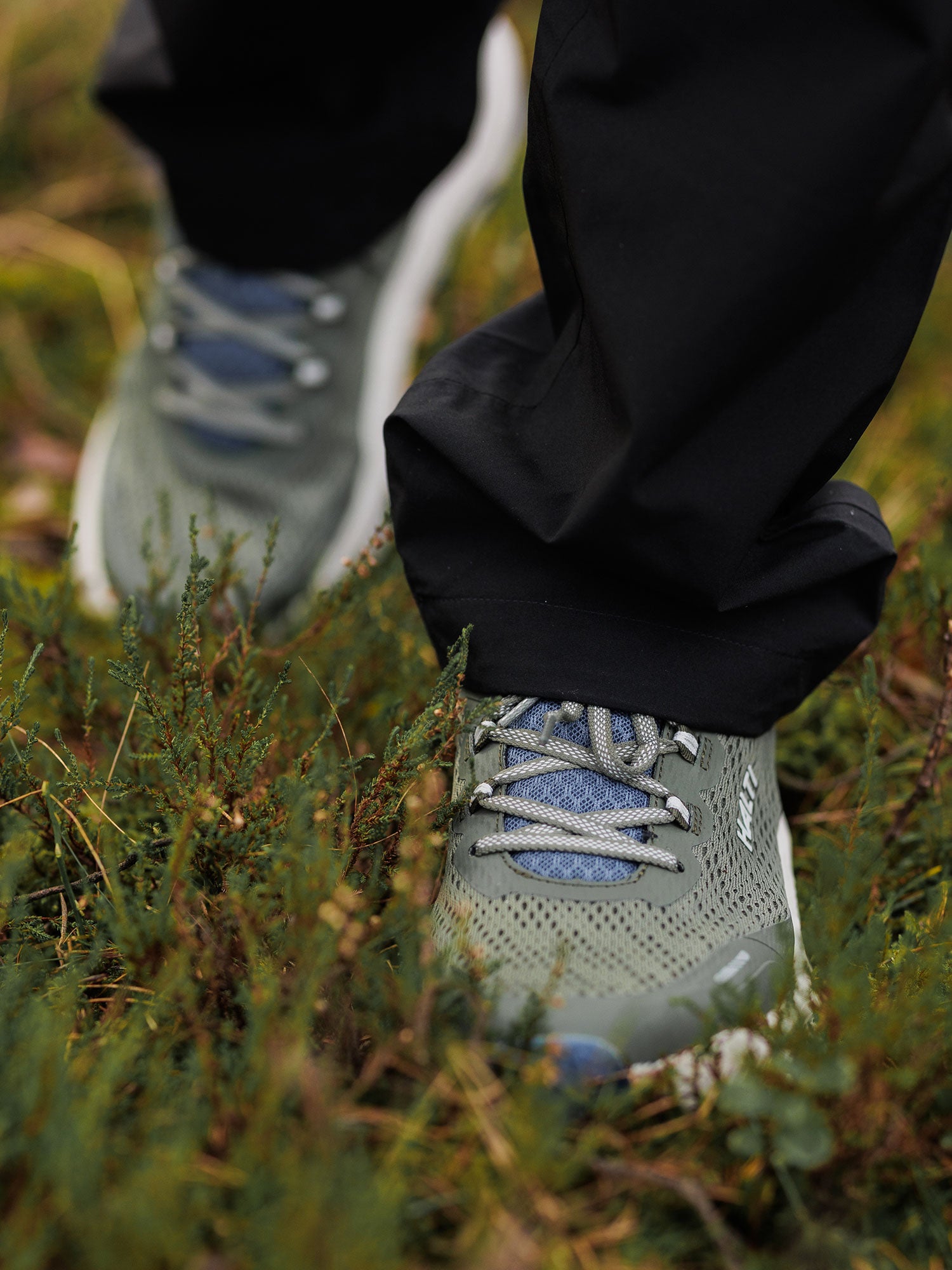 Ein Mann trägt Halti Rapid 2 Sneaker Herren und schwarze Hose auf grünem Gras im Freien.
