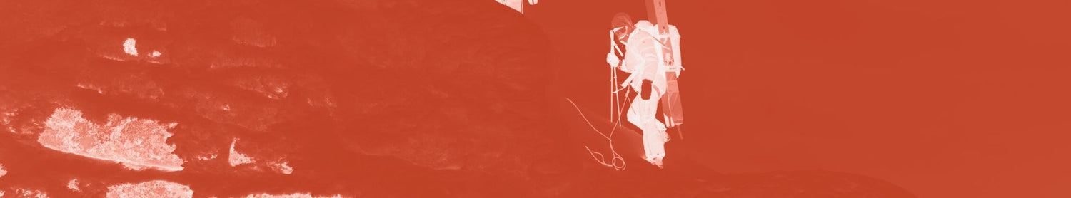 Eine Person klettert an Seilen befestigt eine Felswand hinauf, dargestellt mit einem monochromen Rotfilter.